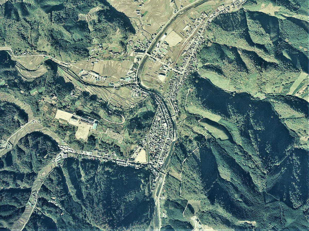 1976年に撮影された西城町中心部の空中写真。川沿いに家並みがあり、周りを山林が囲む