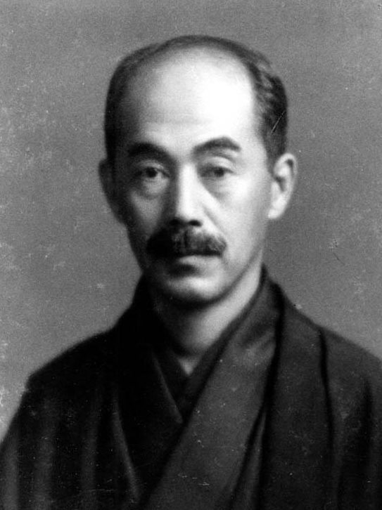 丸い眼鏡をかけ、着物姿で正面を向く年配の男性の肖像写真