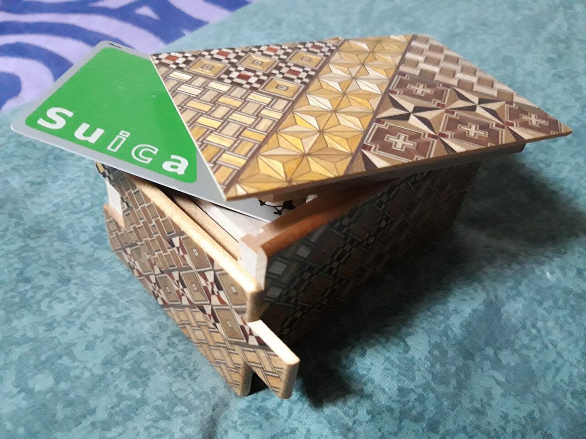 側面をずらして開けた寄木細工の秘密箱。大きさの目安にICカードが置かれている