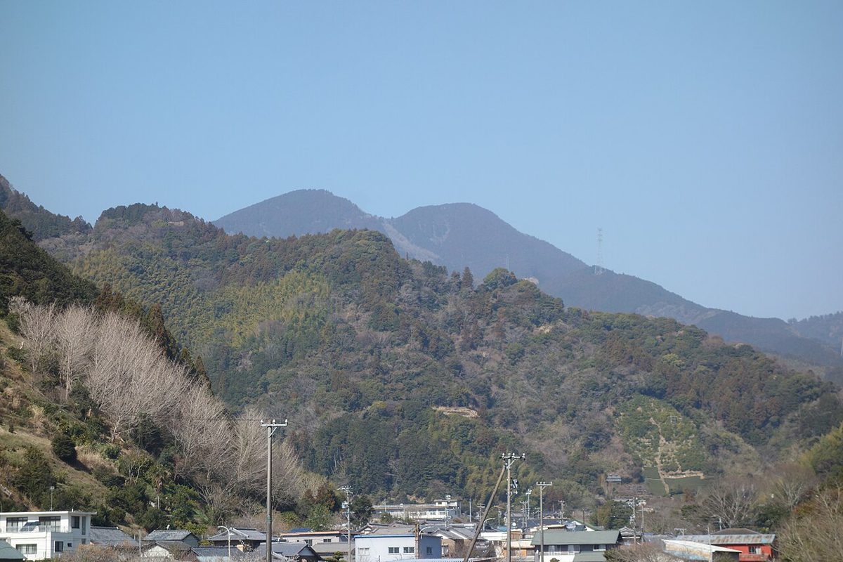 手前に家並みと雑木の山、その奥に二つの峰が並ぶ青空の山の風景