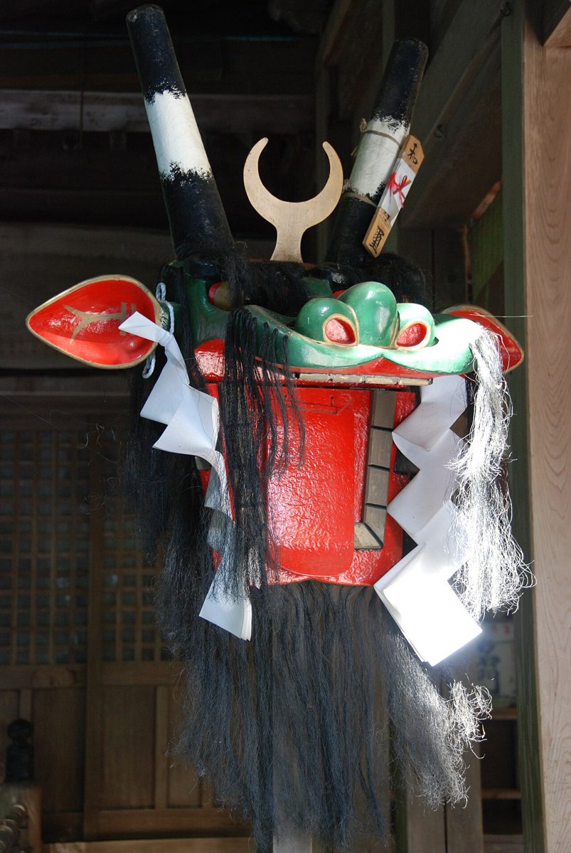 赤い顔に長い黒毛、二本の角をもつ大きな牛鬼の頭が、神社の柱に掛けられている
